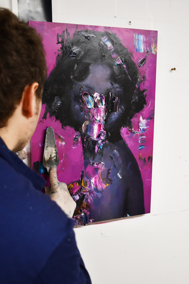 Artist Jean‑Luc Almond stands in his studio applying thick impasto strokes to a figurative oil portrait, textures and bold pigment blending on wood panel.