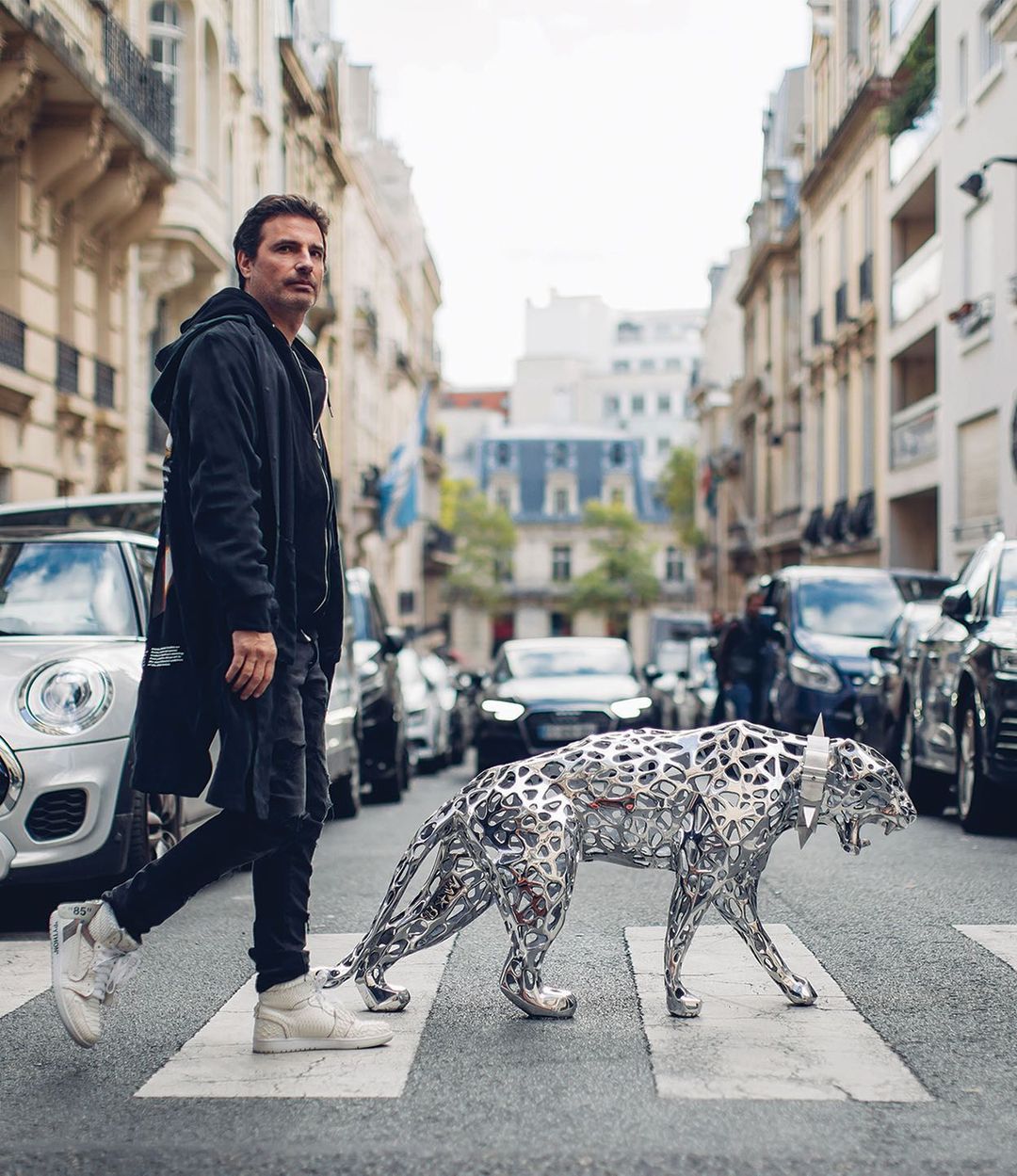 Richard Orlinski walking beside his silver Lace Pantha sculpture in a Parisian street