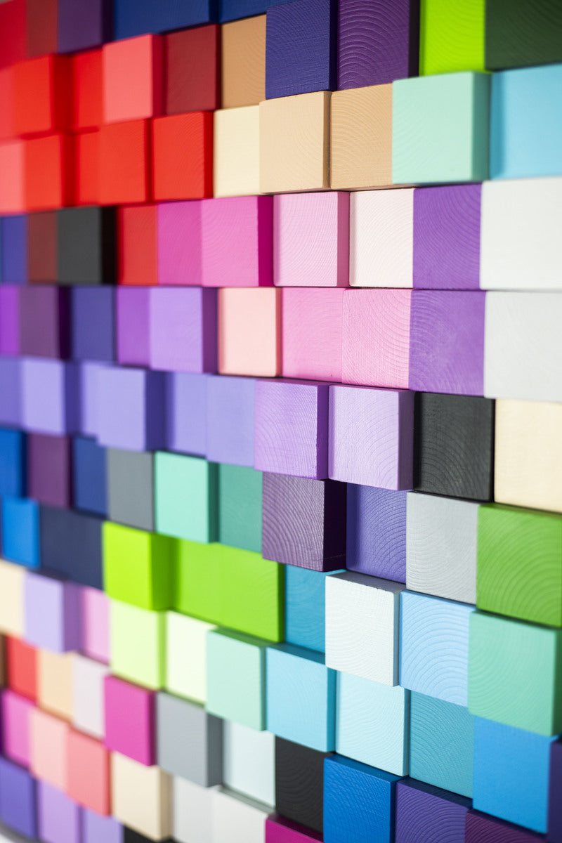 Close-up view of a vibrant geometric wall sculpture by Curtains, featuring multicoloured wooden blocks arranged in a staggered grid pattern.