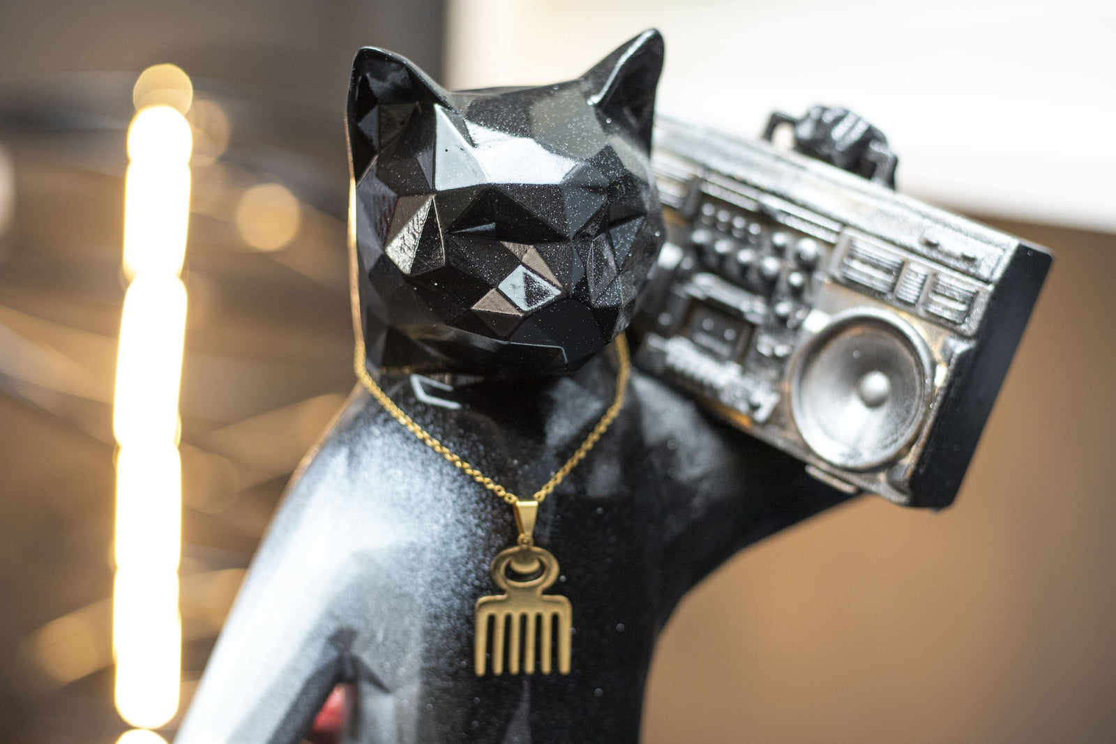 Glossy black geometric cat sculpture from Maxim’s Noisy Rebel collection, wearing a gold necklace and carrying a boombox on its shoulder.