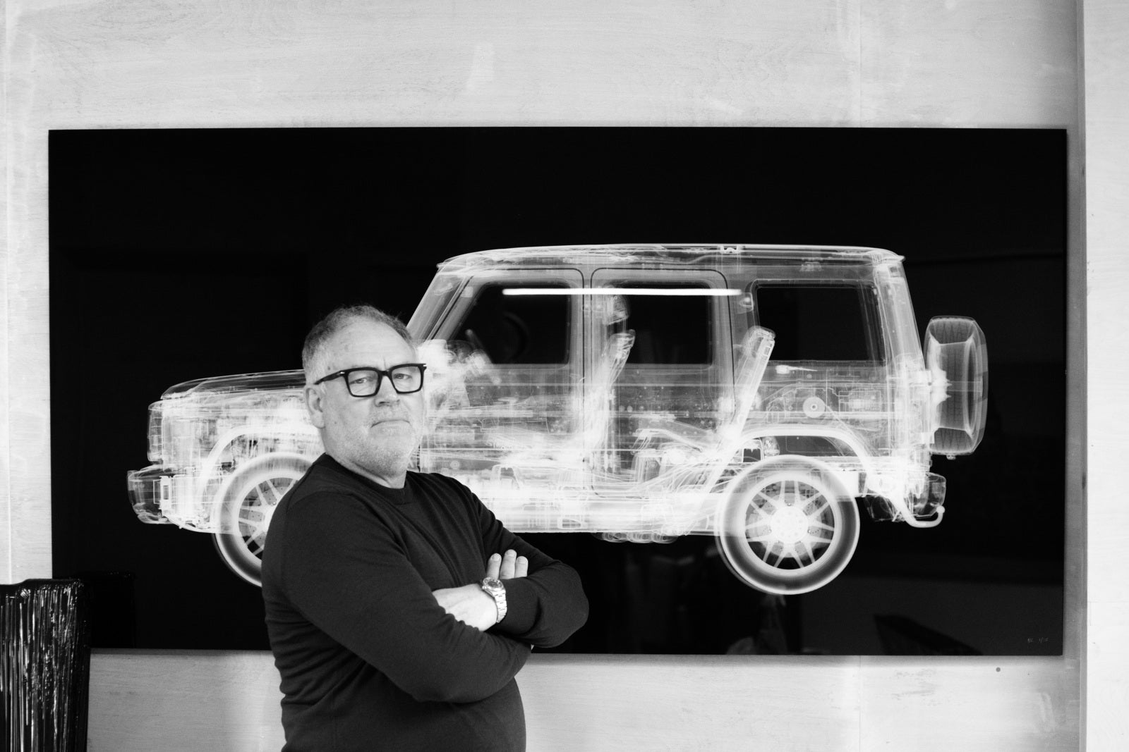 Nick Veasey standing with arms crossed in front of one of his iconic x-ray artworks, a black-and-white image of a 4x4 vehicle.