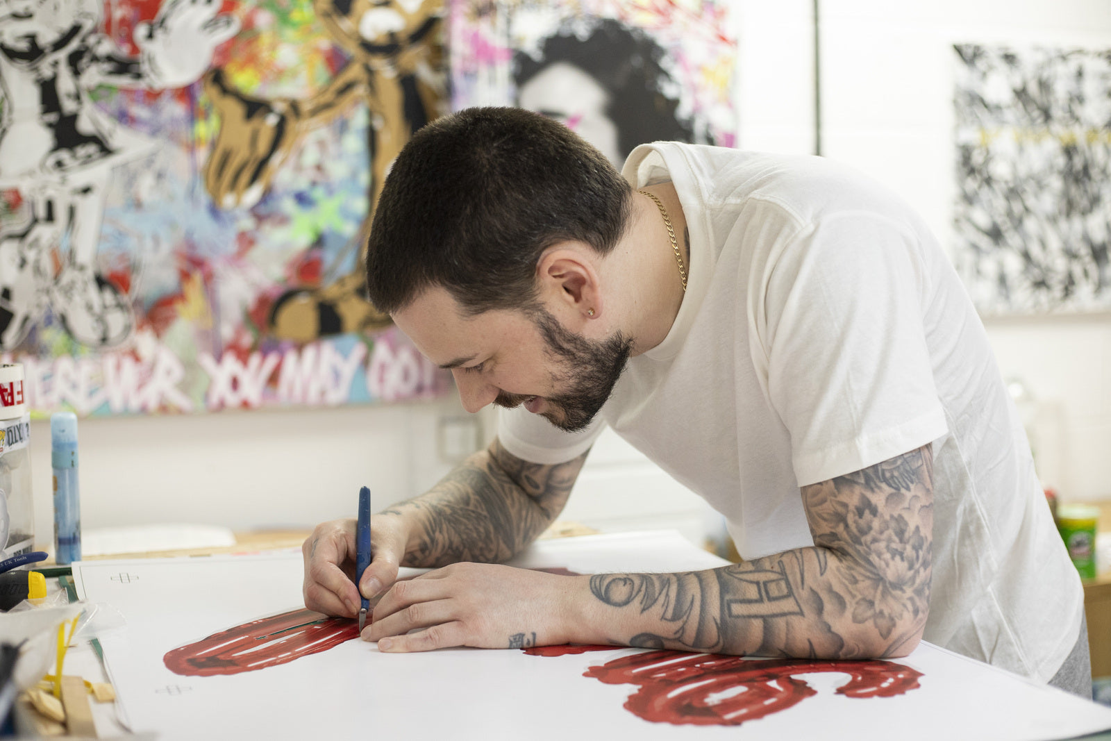 And Wot artist working in his studio, drawing red graffiti-style typography on a canvas with urban artworks in the background