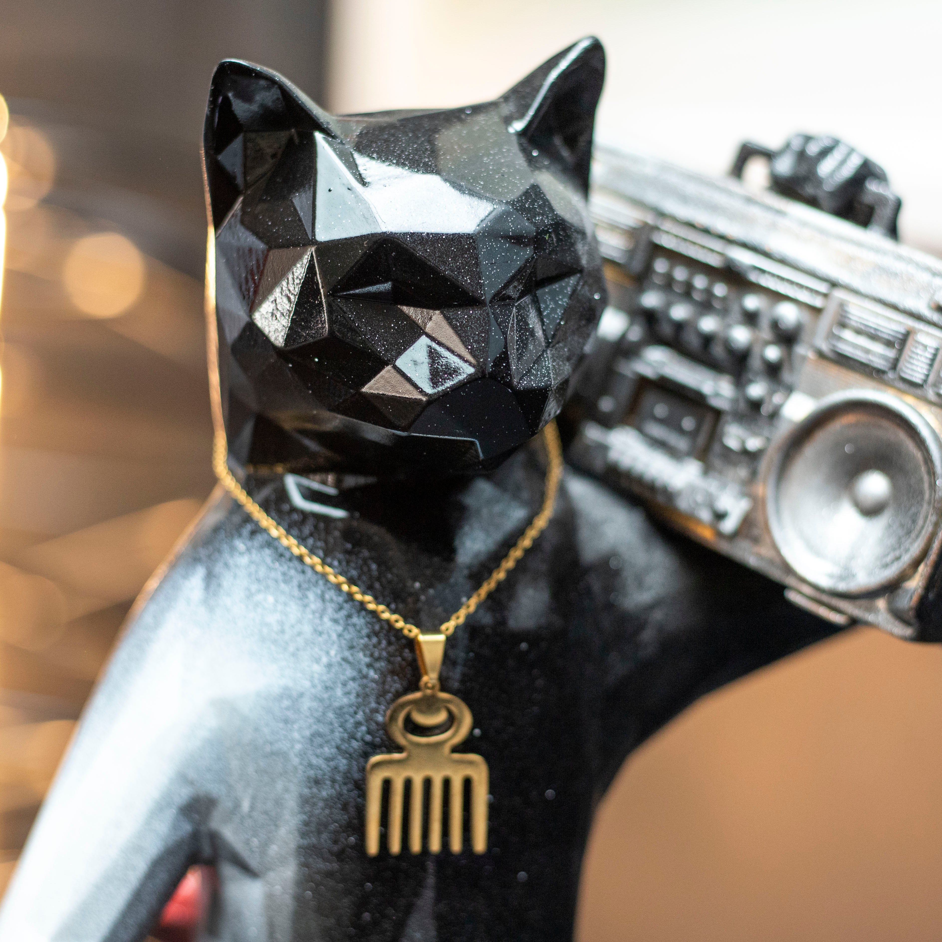 Black cat figurine with a gold necklace holding a silver boombox against a blurred background